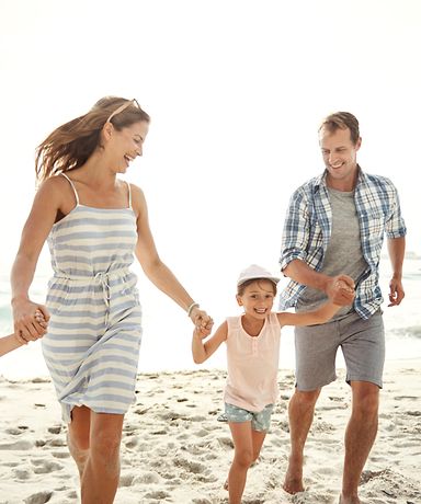 Mutter, Vater und deren zwei Kinder gehen am Strand spazieren und lachen. 