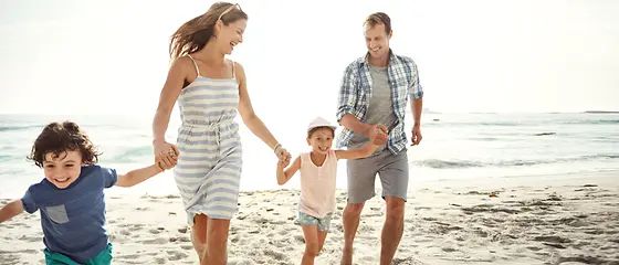 Mutter, Vater und deren zwei Kinder gehen am Strand spazieren und lachen. 