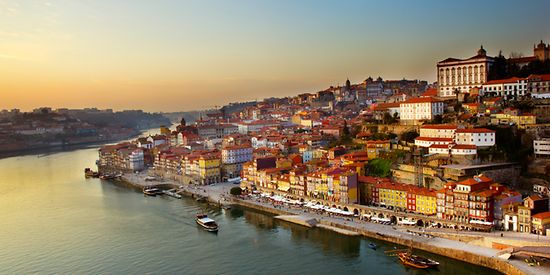 Man sieht einen Hügel mit der Altstadt von Porto. Im Vordergrund ist ein Fluss zu sehen.