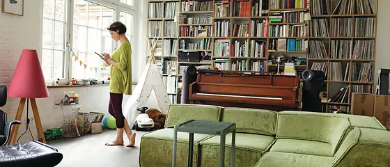 Frau schaut aus ihrem Fenster mit dem versicherten Hausrat im Hintergrund