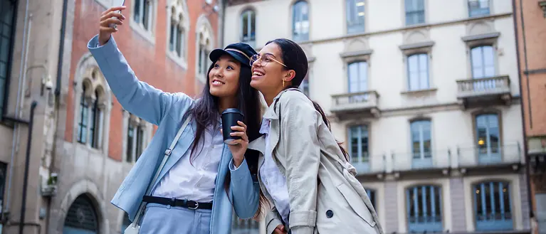 Due donne in piedi in città si scattano un selfie