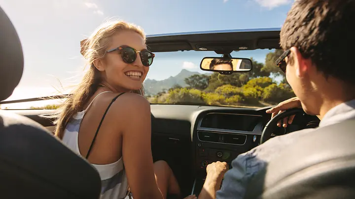 Due persone sedute nella decappottabile, la donna ride davanti alla telecamera