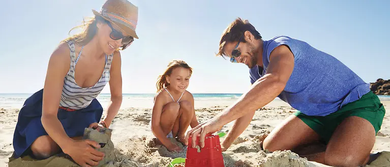 Una famiglia con un bambino si siede sulla spiaggia e costruisce insieme castelli di sabbia