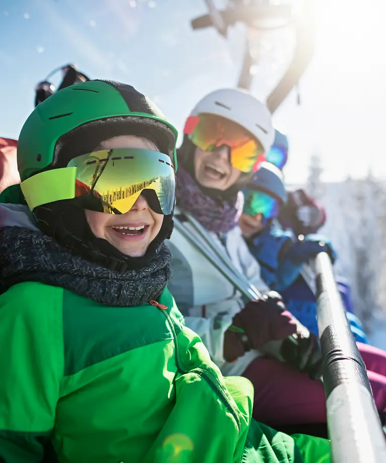 Eine Familie sitzt im Skilift. Im Hintergrund sind verschneite Bäume zusehen. 